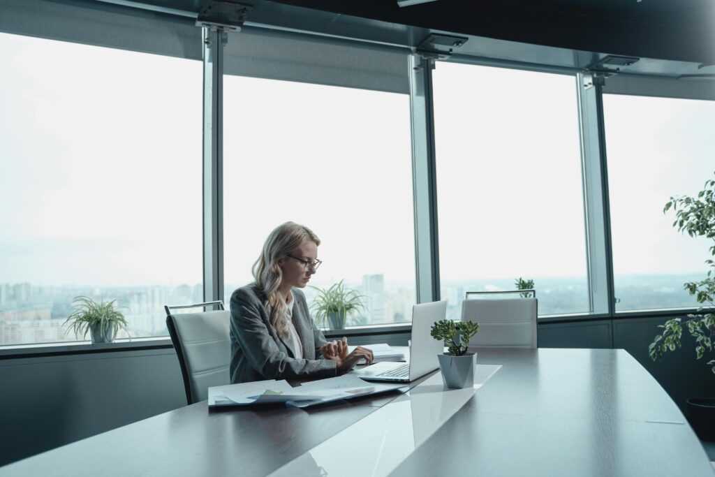 Woman with laptop working in a bright, modern office with large windows.