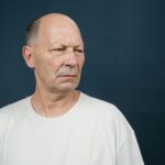 Thoughtful senior man in white shirt against a dark background, studio portrait.